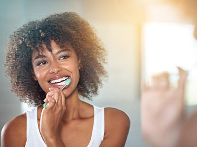 Woman with curly hair brushing teeth in front of mirror