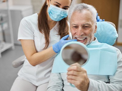 Man in dental chair looking into mirror with dentist touching his teeth