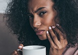 Woman with coffee cup holding jaw