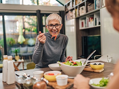 Woman with black glasses smiling while eating with friend