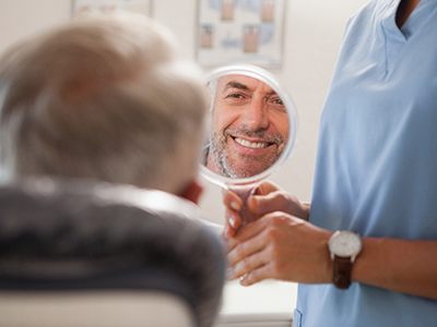 Man smiling at reflection in handheld mirror
