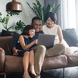 a family sitting on a couch together and looking at a laptop