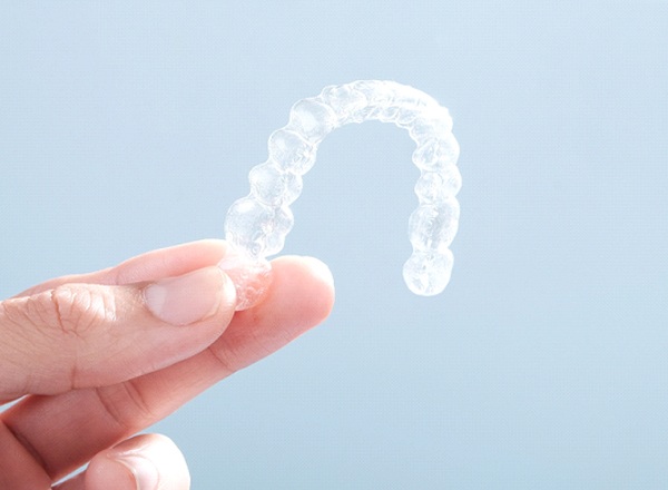 Close-up of hand holding an Invisalign aligner on plain background