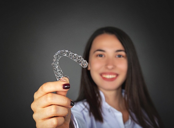 Happy woman smiling and holding Invisalign on black background