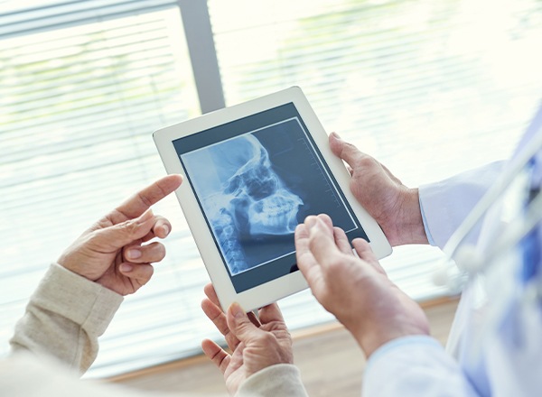 Dentist looking at patient chart and digital x0rays of jaw and skull