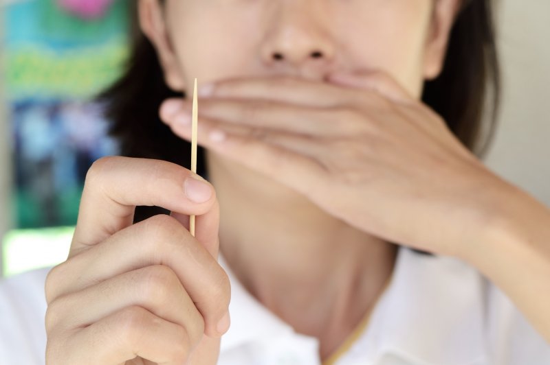 Picture of someone holding a toothpick and covering their mouth