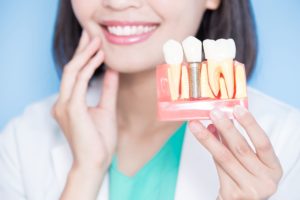 Dentist holding her fingers to her jaw with one hand and a model dental implant in the other