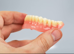 Hand holding full denture for lower arch